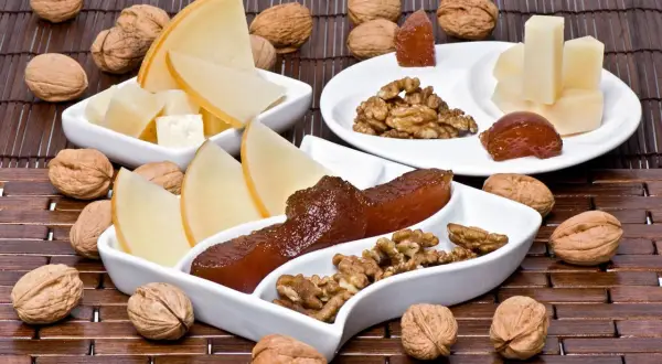 Queso y nueces acompañan trozos de dulce de manzana en una tabla de madera.