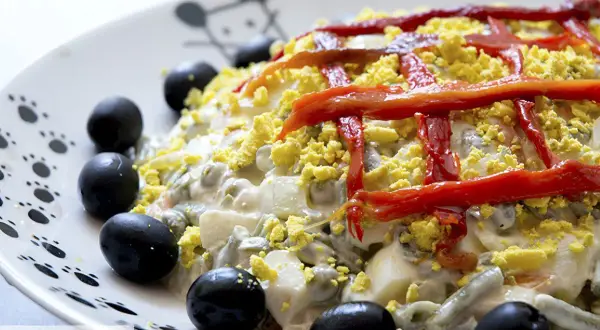 Ensaladilla rusa Thermomix cremosa, decorada con pimientos rojos y aceitunas negras. ¡Perfecta para cualquier ocasión!
