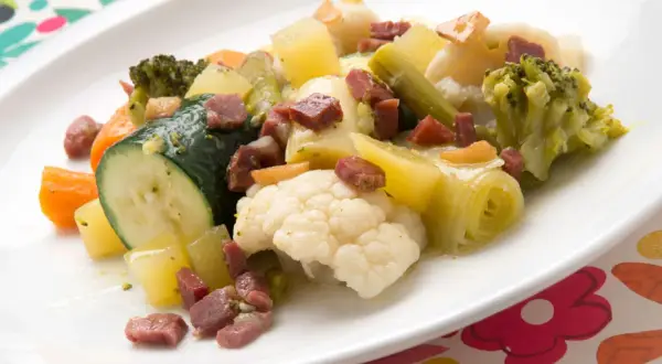 Un colorido panache de verduras con brócoli, coliflor, calabacín, zanahoria y patatas, salpicado de trocitos de jamón.