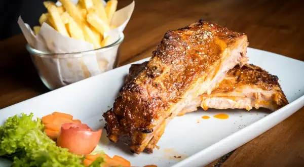 Costillas de cerdo al horno jugosas y doradas, acompañadas de papas fritas crujientes y una guarnición fresca.