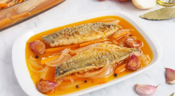 Dos filetes de caballa en escabeche, con zanahoria, cebolla y ajos en una salsa dorada.