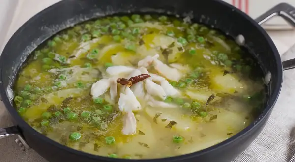 Patatas en salsa verde con trozos de pescado blanco y guisantes, servido en una sartén negra.