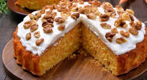 Un delicioso bizcocho de zanahoria, cubierto con glaseado blanco y nueces, servido en una tabla de madera.