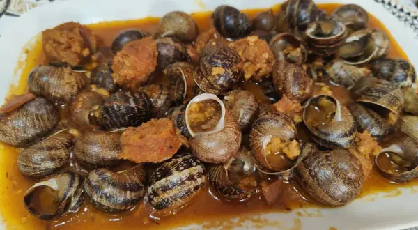 Un plato abundante de caracoles en salsa, con trozos de chorizo y especias, listo para disfrutar.