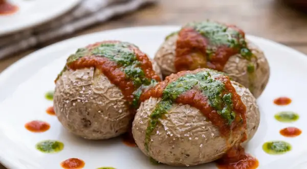 Tres papas arrugadas con mojo rojo y verde, sal marina y puntos de salsa en un plato blanco.