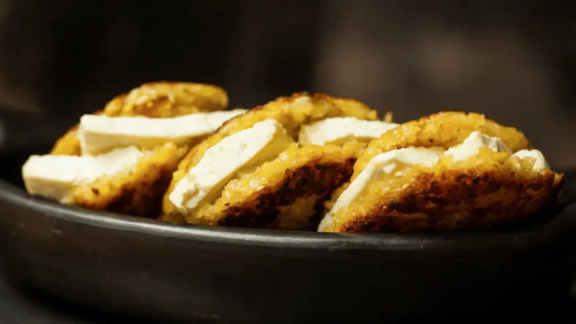 Arepas de choclo doradas y crujientes, rellenas de queso blanco fresco, servidas en un cuenco de barro.