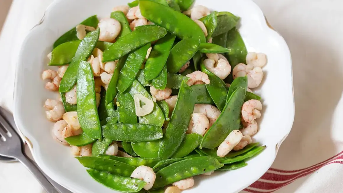 Plato de tirabeques salteados con gambas y ajo. Los tirabeques, crujientes y verdes, se mezclan con las gambas rosadas y láminas de ajo.