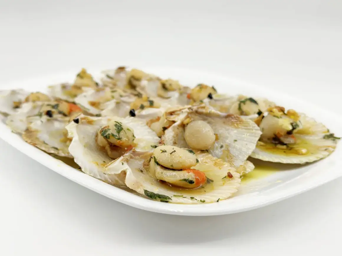Zamburiñas a la plancha, jugosas y doradas, servidas en su concha con perejil picado y un toque de ajo.