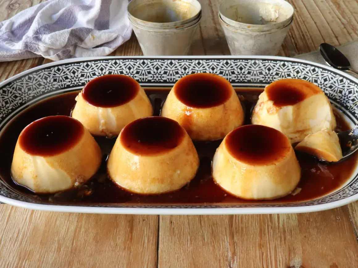 Seis deliciosos flanes de leche condensada, bañados en caramelo oscuro, servidos en una bandeja decorada.