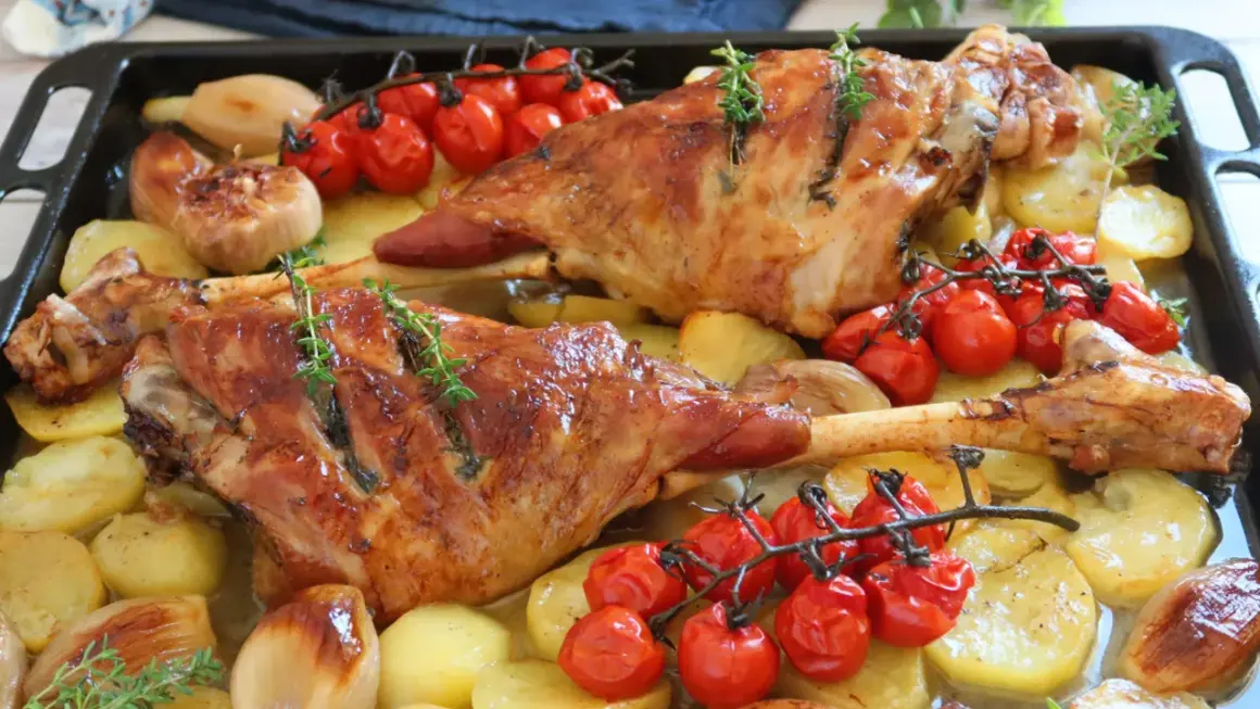 Pierna de cordero al horno jugosa, con patatas, tomates cherry y cebolla. ¡Un festín para los sentidos!