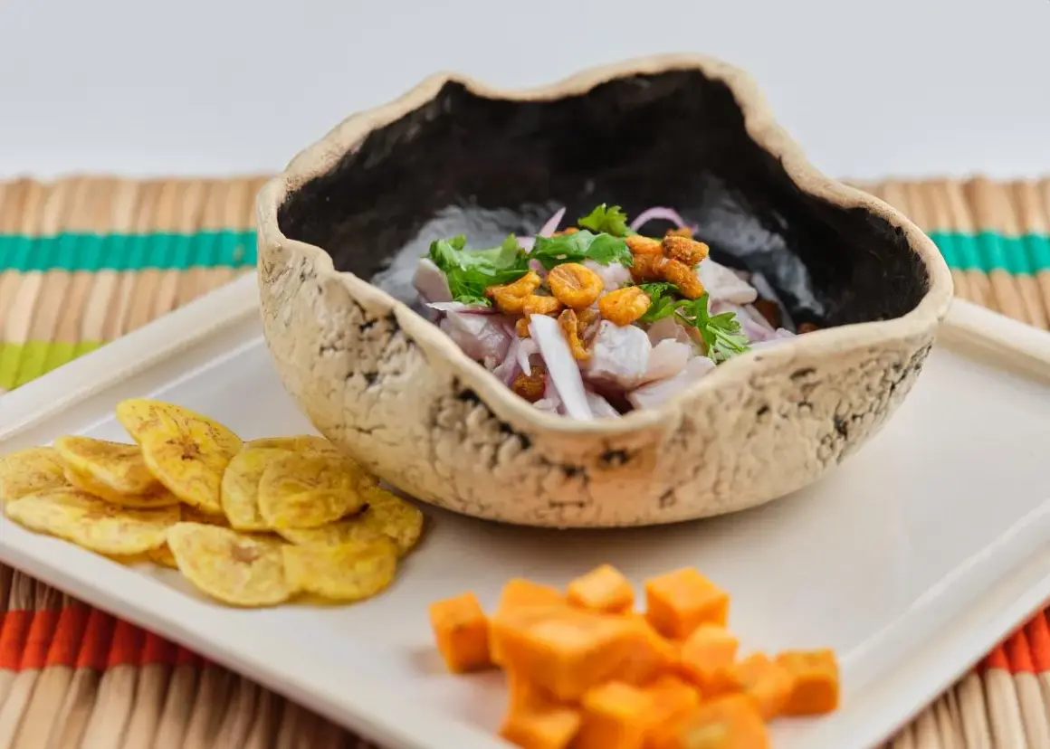 Delicioso ceviche de corvina en cuenco rústico, acompañado de patacones y cubos de camote.
