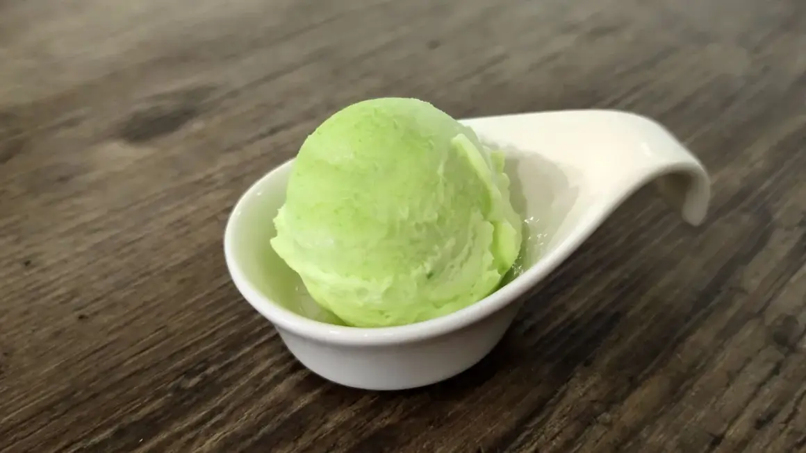 Una bola de helado de manzana verde en un cuenco blanco sobre una mesa de madera.