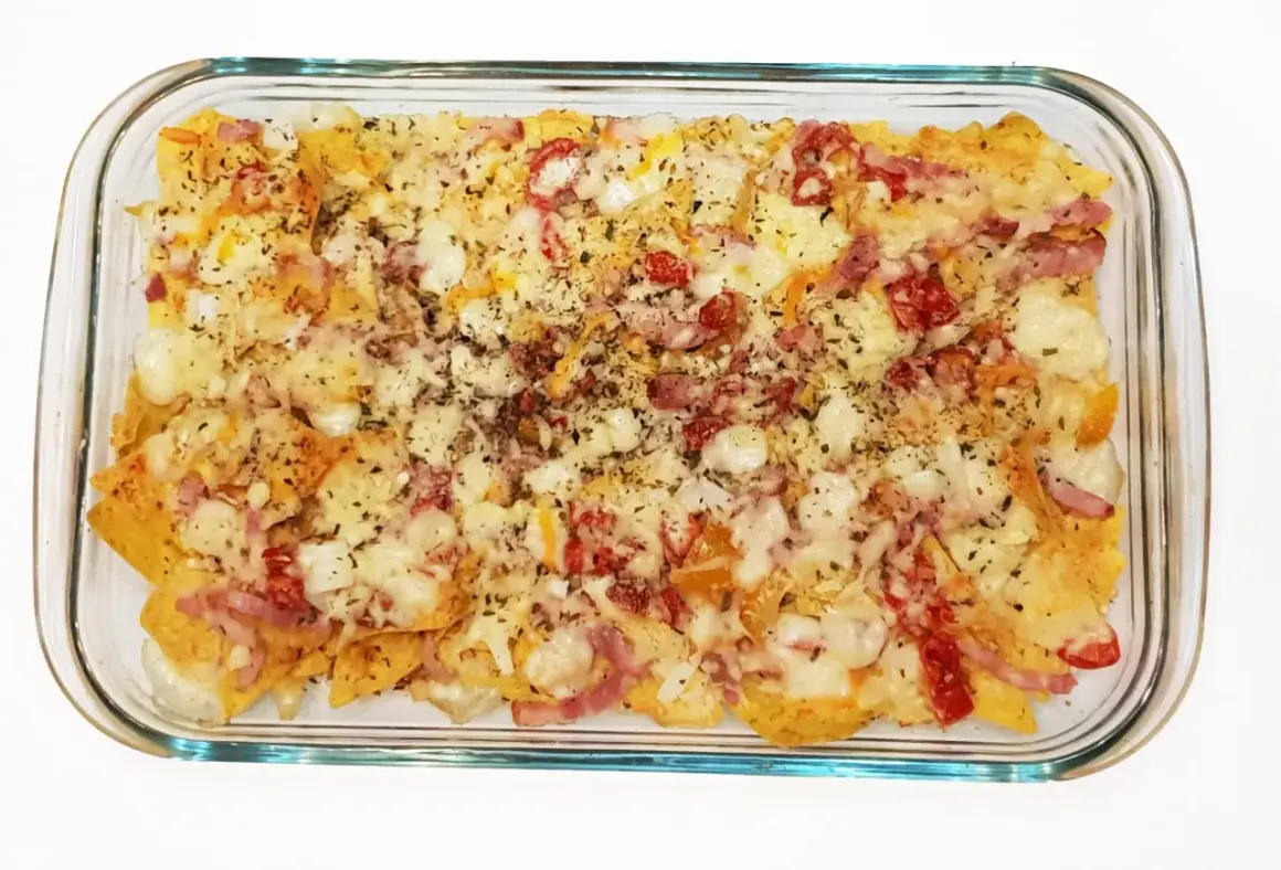 Nachos con queso horneados, cubiertos con trozos de tocino y pimientos rojos.