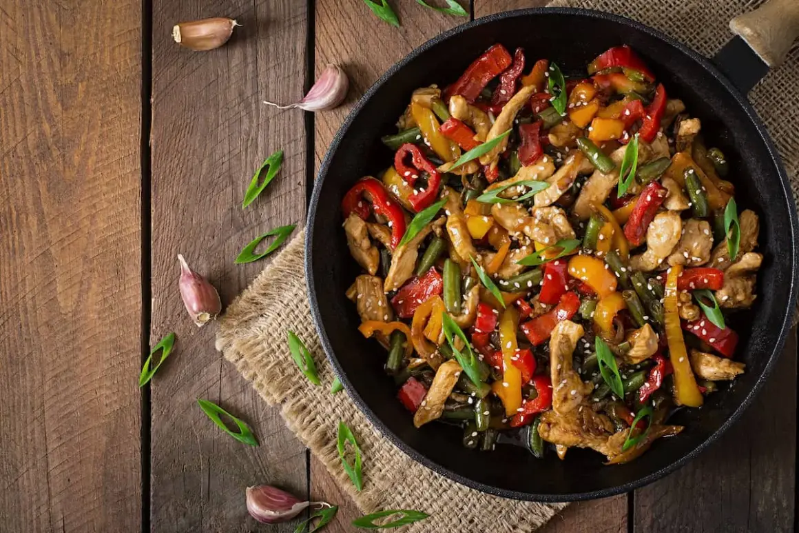 Wok de pollo con pimientos de colores y judías verdes, espolvoreado con sésamo y cebolleta.