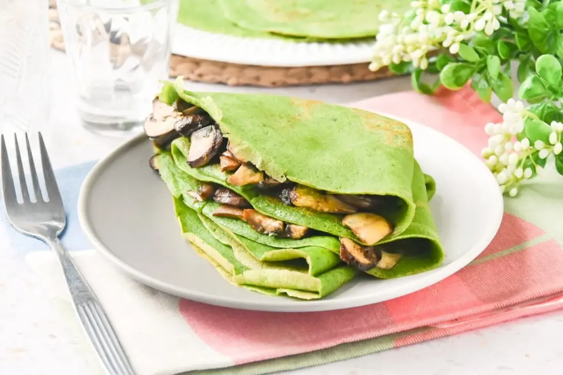 Deliciosos crepes de espinacas rellenos de champiñones salteados, servidos en un plato gris con un tenedor al lado.