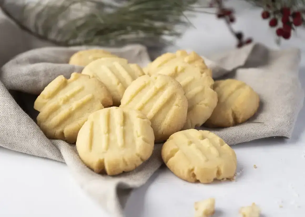 Montón de galletas de mantequilla doradas con líneas marcadas, servidas sobre una tela gris.