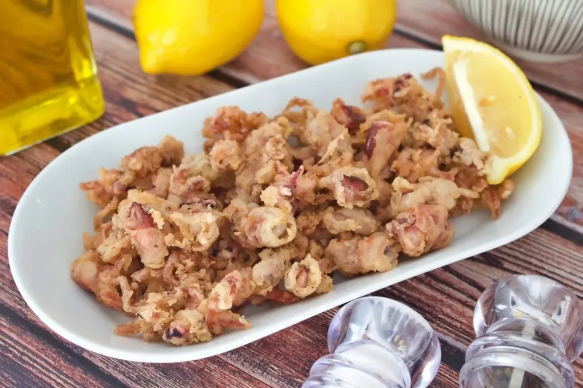 Crujientes puntillas de calamar fritas en un plato blanco, acompañadas de limón, aceite y saleros.