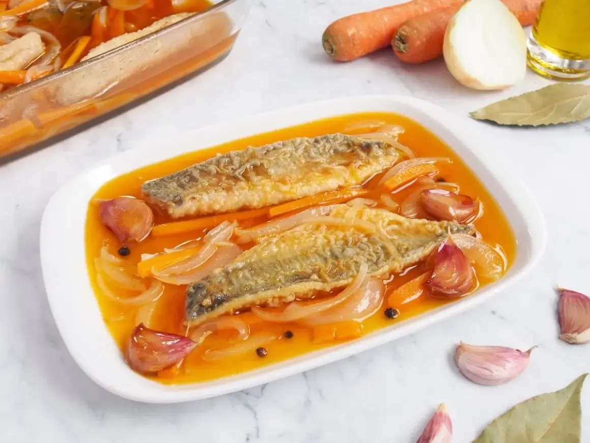 Dos filetes de caballa en escabeche, con zanahoria, cebolla y ajos en una salsa dorada.