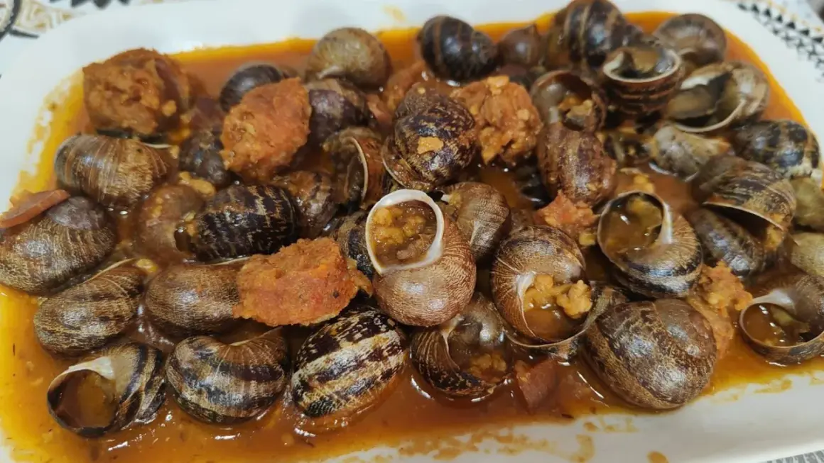 Un plato abundante de caracoles en salsa, con trozos de chorizo y especias, listo para disfrutar.