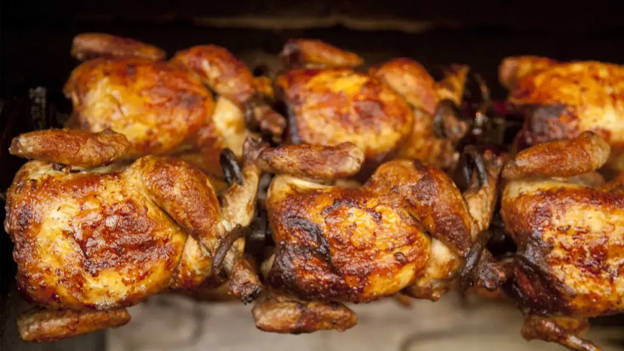 Pollos dorados y jugosos girando en el asador, listos para ser servidos como un delicioso pollo a la brasa.