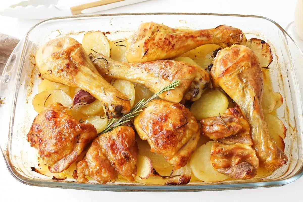 Pollo al horno dorado y jugoso con patatas asadas, romero y ajos en una bandeja de cristal. ¡Un festín casero!