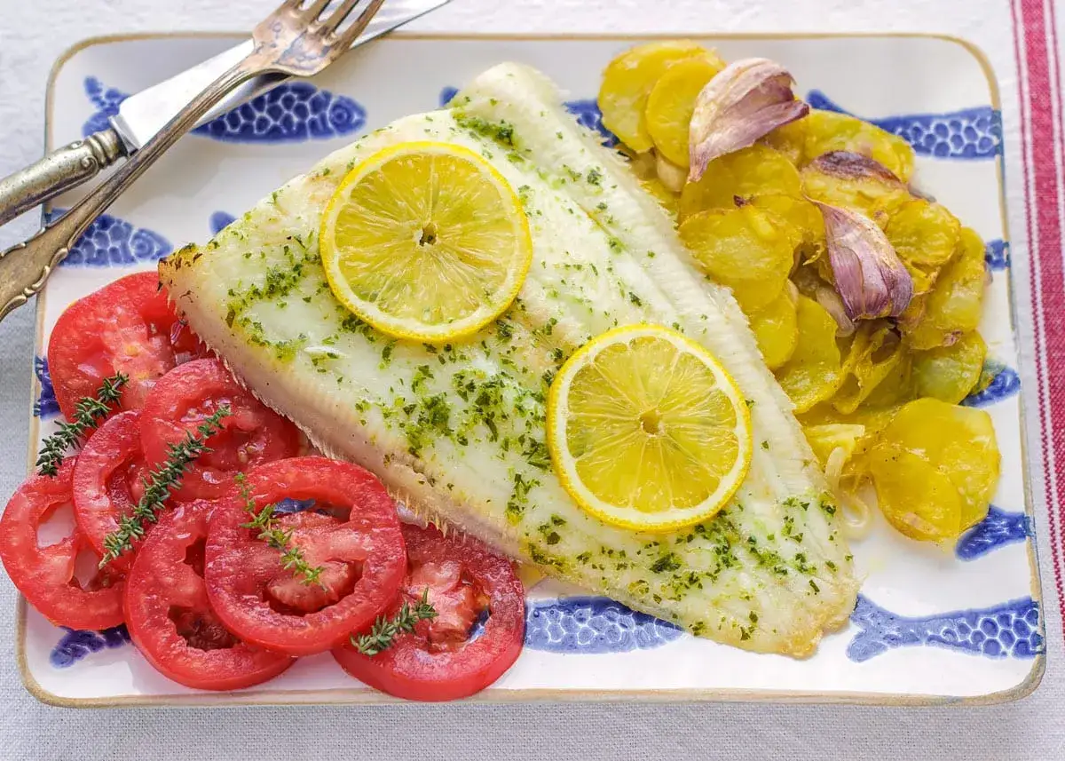 Delicioso lenguado al horno con rodajas de limón, tomates frescos y patatas asadas.
