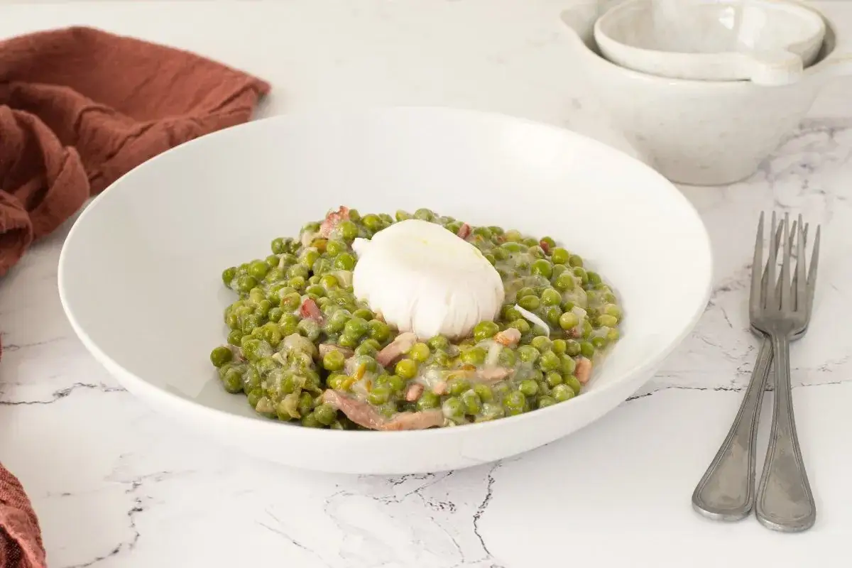 Un plato de guisantes a la francesa cremosos con trocitos de panceta y un huevo escalfado encima.