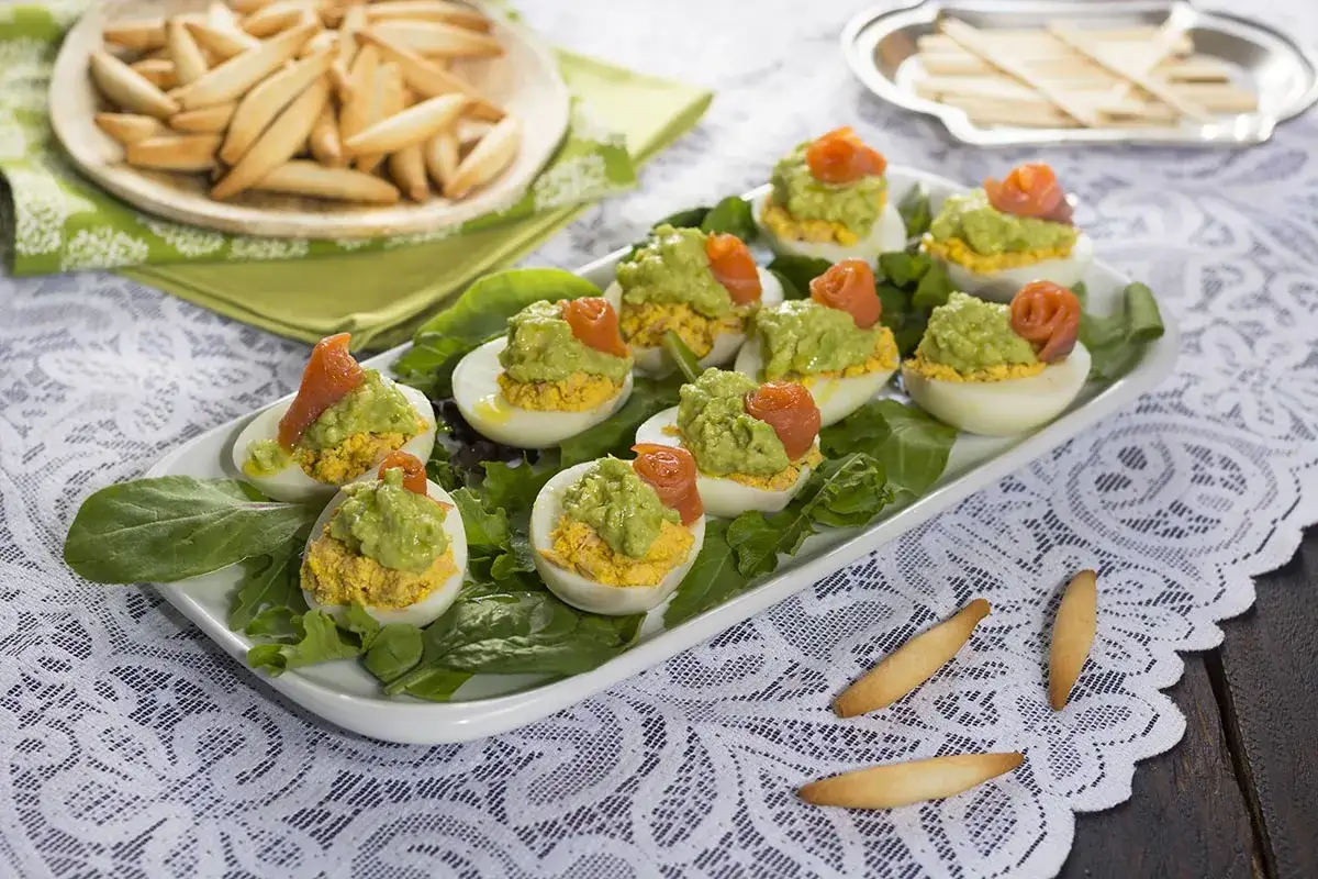 Deliciosos huevos rellenos de aguacate y salmón, servidos sobre hojas verdes. Un aperitivo perfecto.