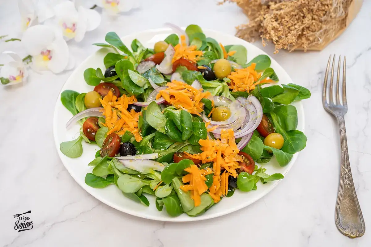 Una ensalada fresca con lechuga, tomate, aceitunas, cebolla morada y zanahoria rallada. Un ejemplo de los muchos tipos de ensaladas saludables.