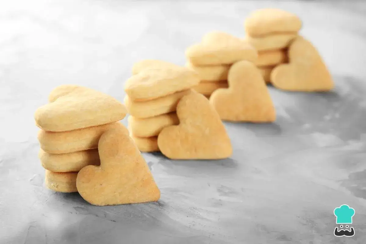 Deliciosas galletas de mantequilla con forma de corazón, apiladas en un fondo gris texturizado.