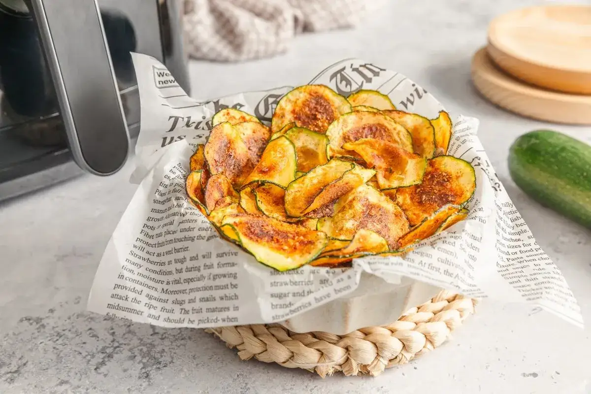 Crujientes rodajas de calabacín en airfryer, servidas sobre papel de periódico. Un snack saludable y delicioso.
