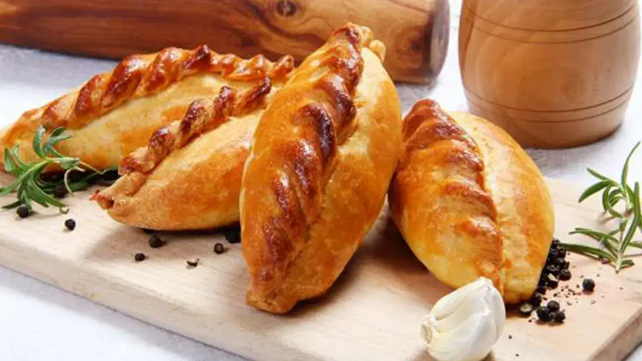 Tres empanadas de carne doradas y crujientes, decoradas con romero y granos de pimienta negra, listas para disfrutar.