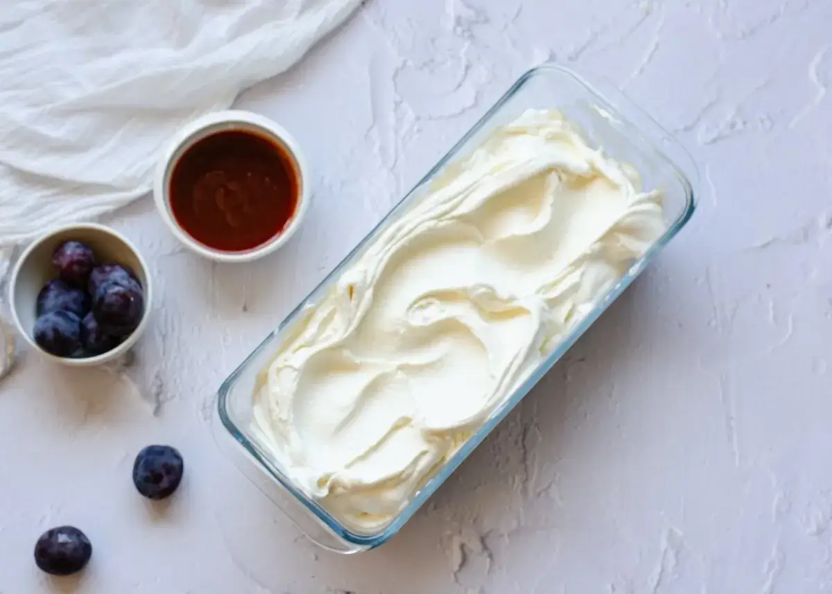 Helado de queso cremoso en un recipiente de vidrio, acompa&ntilde;ado de ciruelas y salsa de caramelo.