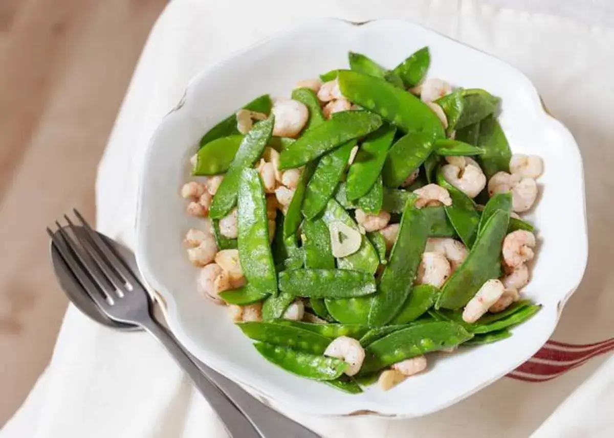 Un plato de tirabeques que son crujientes y sabrosos, mezclados con camarones rosados y trozos de ajo.