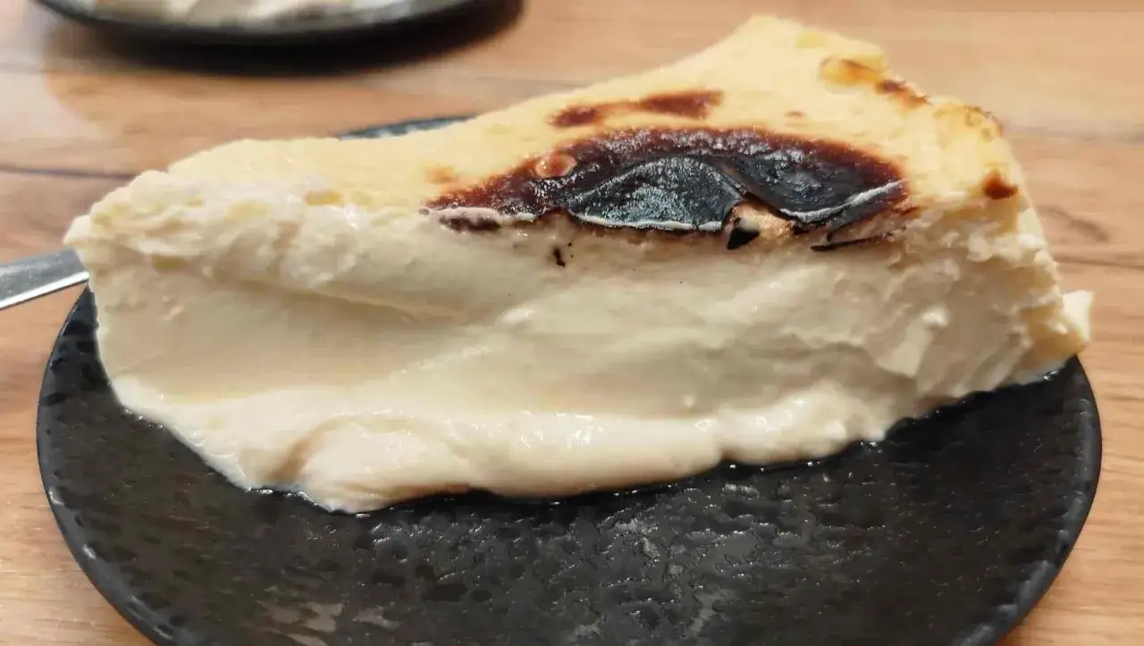 Tarta de queso cremosa, con el toque quemado caracter&iacute;stico de la tarta de queso Eva Argui&ntilde;ano, servida en plato negro.