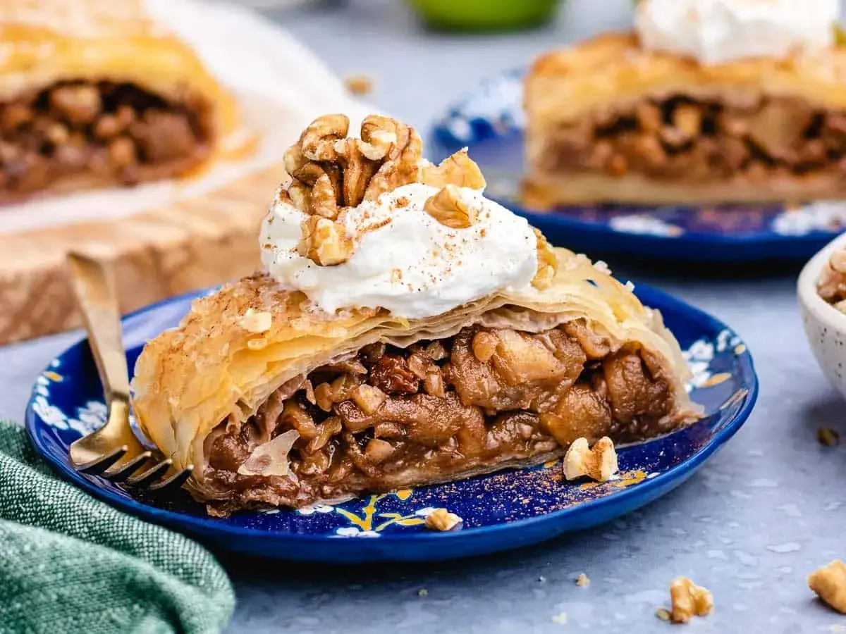 Delicioso strudel de manzana con crema batida y nueces, servido en un plato azul.