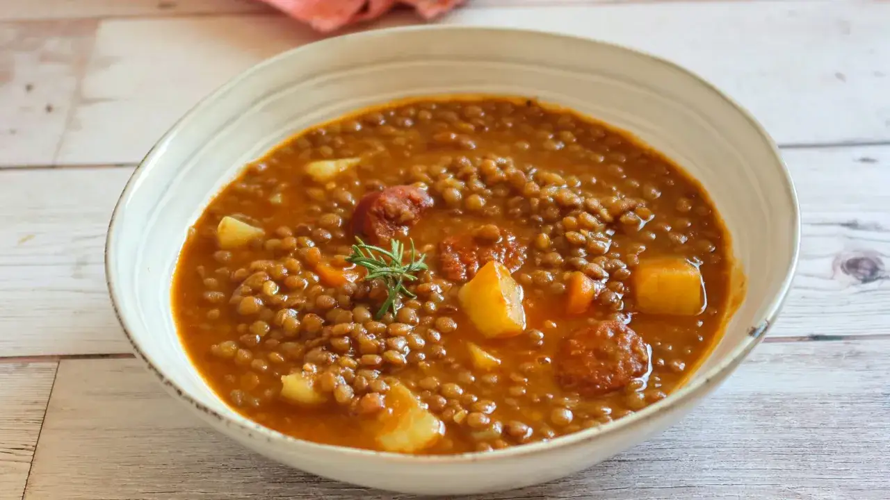 Un plato humeante de lentejas con chorizo, patatas y zanahorias, decorado con romero.