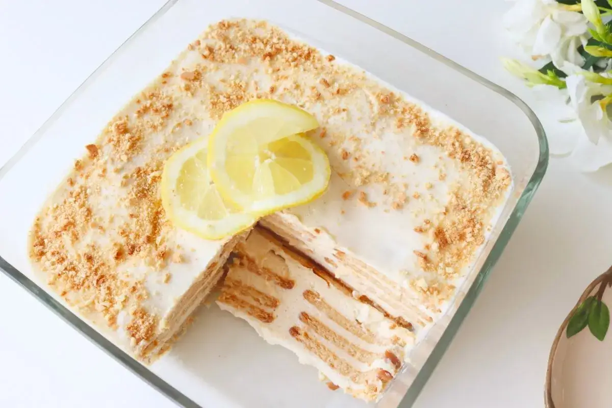 Deliciosa carlota de limón en un molde de vidrio, decorada con rodajas de limón y migas de galleta.