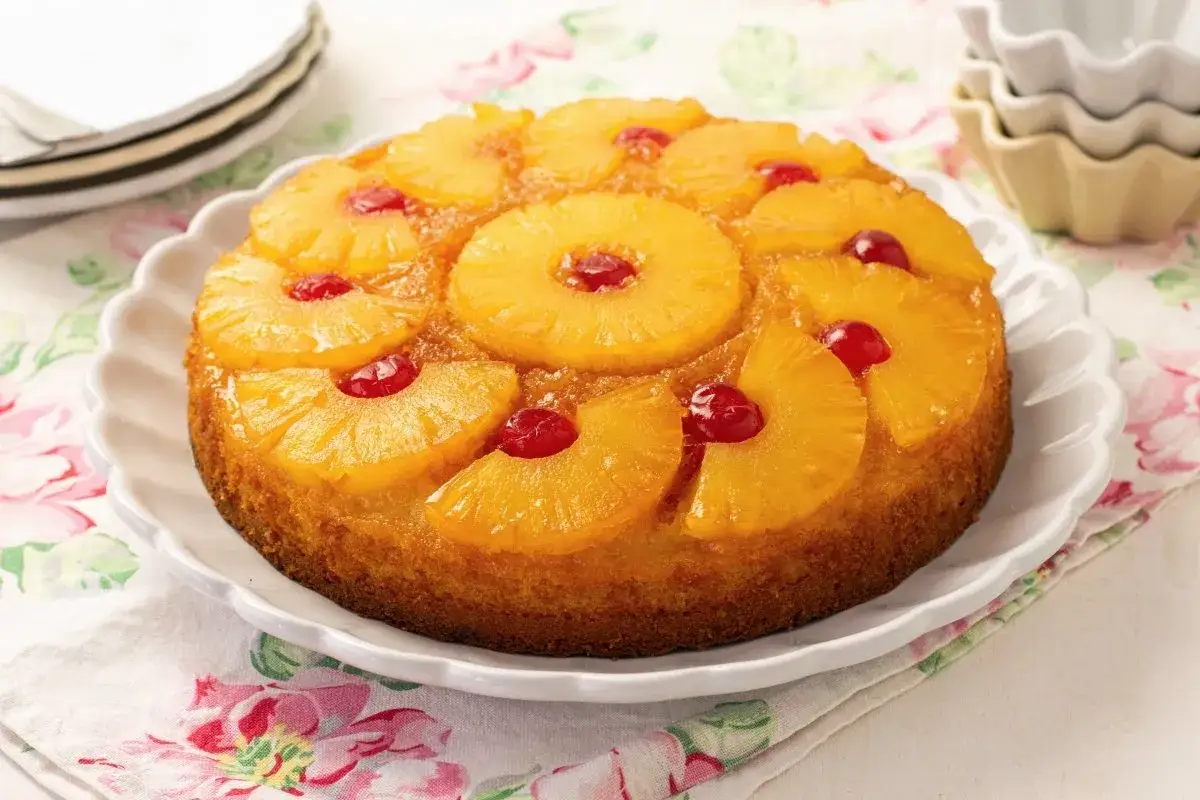 Tarta de pi&ntilde;a dorada y jugosa, decorada con rodajas de pi&ntilde;a y cerezas rojas. Un cl&aacute;sico postre que evoca dulces recuerdos.