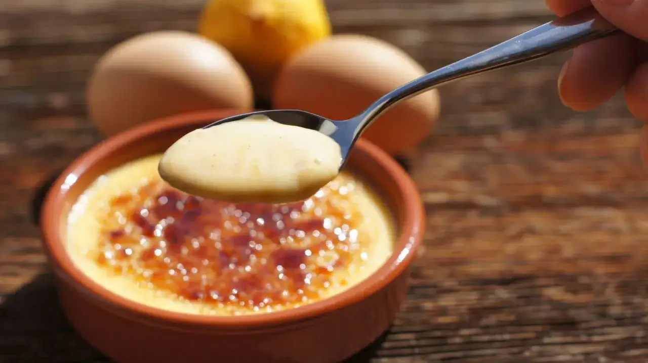 Cuchara con deliciosa crema catalana, lista para ser disfrutada. Huevos y limón al fondo.