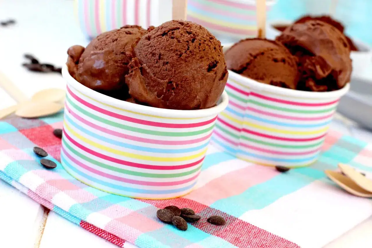 Dos copas de helado de chocolate casero con chispas de chocolate y cucharas de madera sobre un mantel a cuadros.