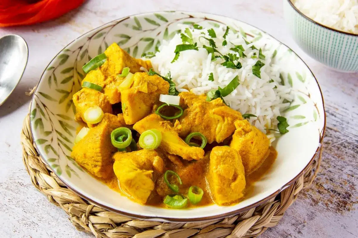 Sabroso pollo al curry con arroz blanco y cebolleta picada, servido en un plato decorado.
