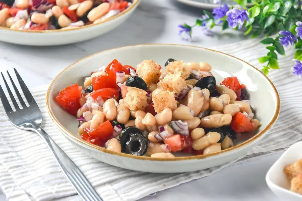 Deliciosa ensalada de judías blancas con tomates, aceitunas negras, cebolla roja y picatostes crujientes.