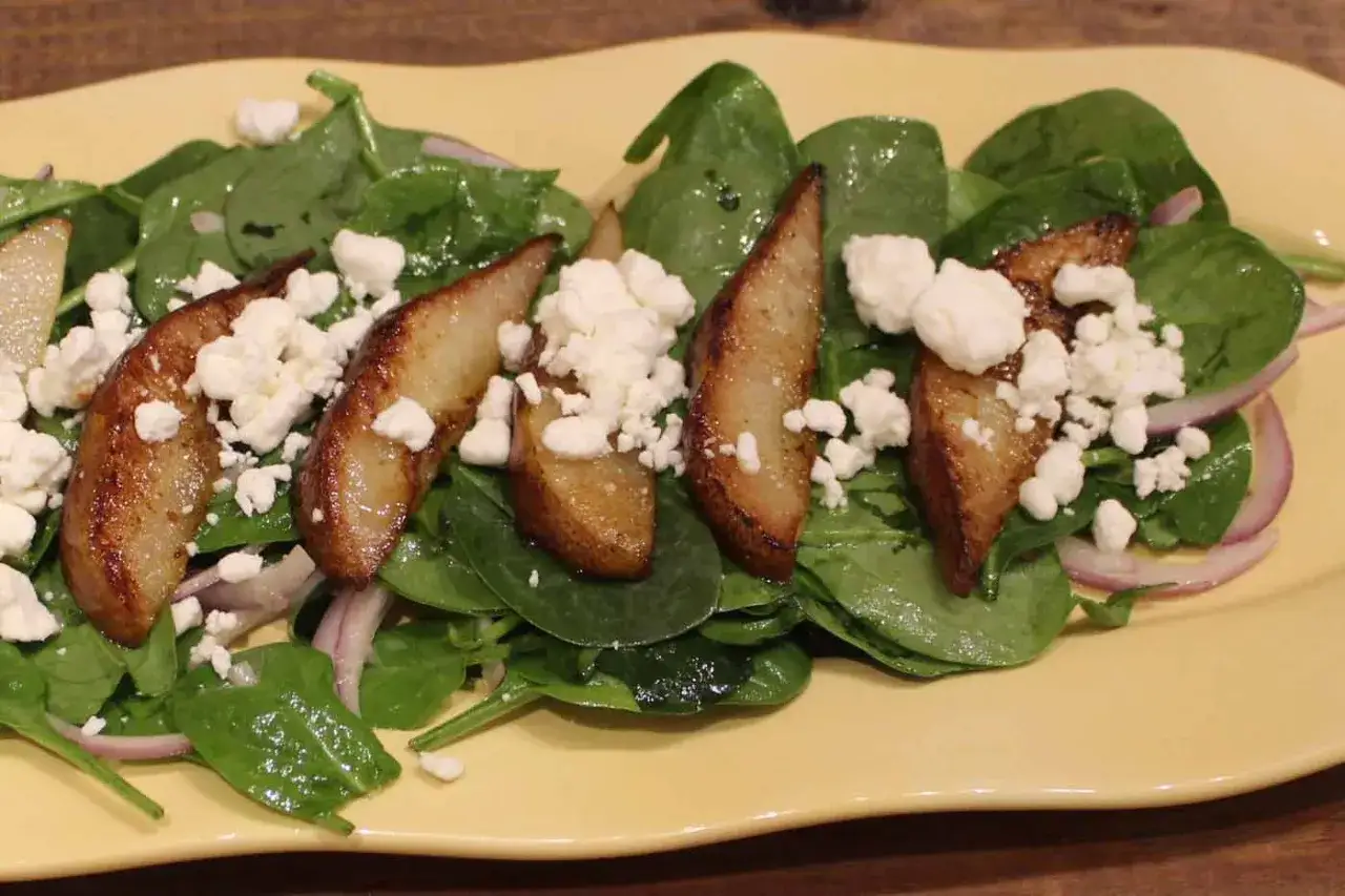 Deliciosa ensalada de espinacas con peras caramelizadas, queso de cabra desmoronado y cebolla morada.
