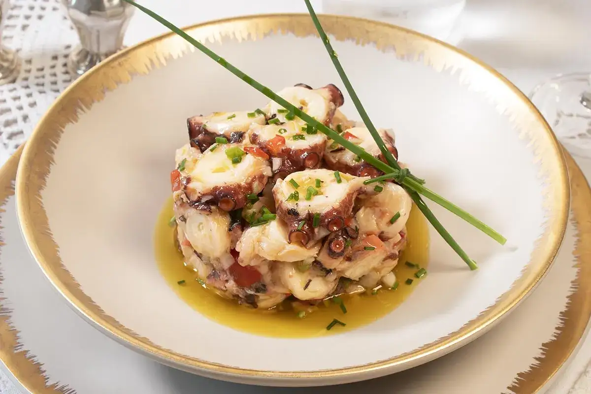 Salpicon de pulpo fresco, con trozos de tomate y cebolla, aderezado con aceite de oliva y guarnición de cebollino.