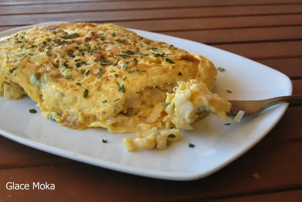 Tortilla de bacalao vasca esponjosa, con trozos de bacalao y perejil picado, servida en plato blanco.
