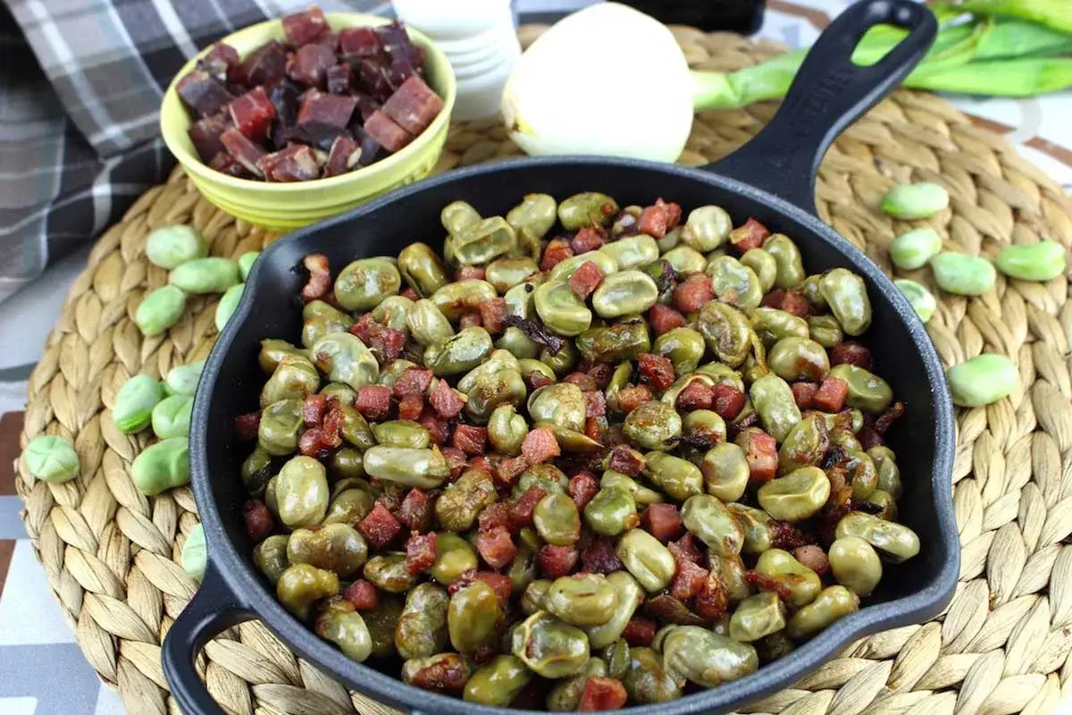 Habas tiernas salteadas con trocitos de jam&oacute;n en una sart&eacute;n de hierro fundido, un plato tradicional y delicioso.