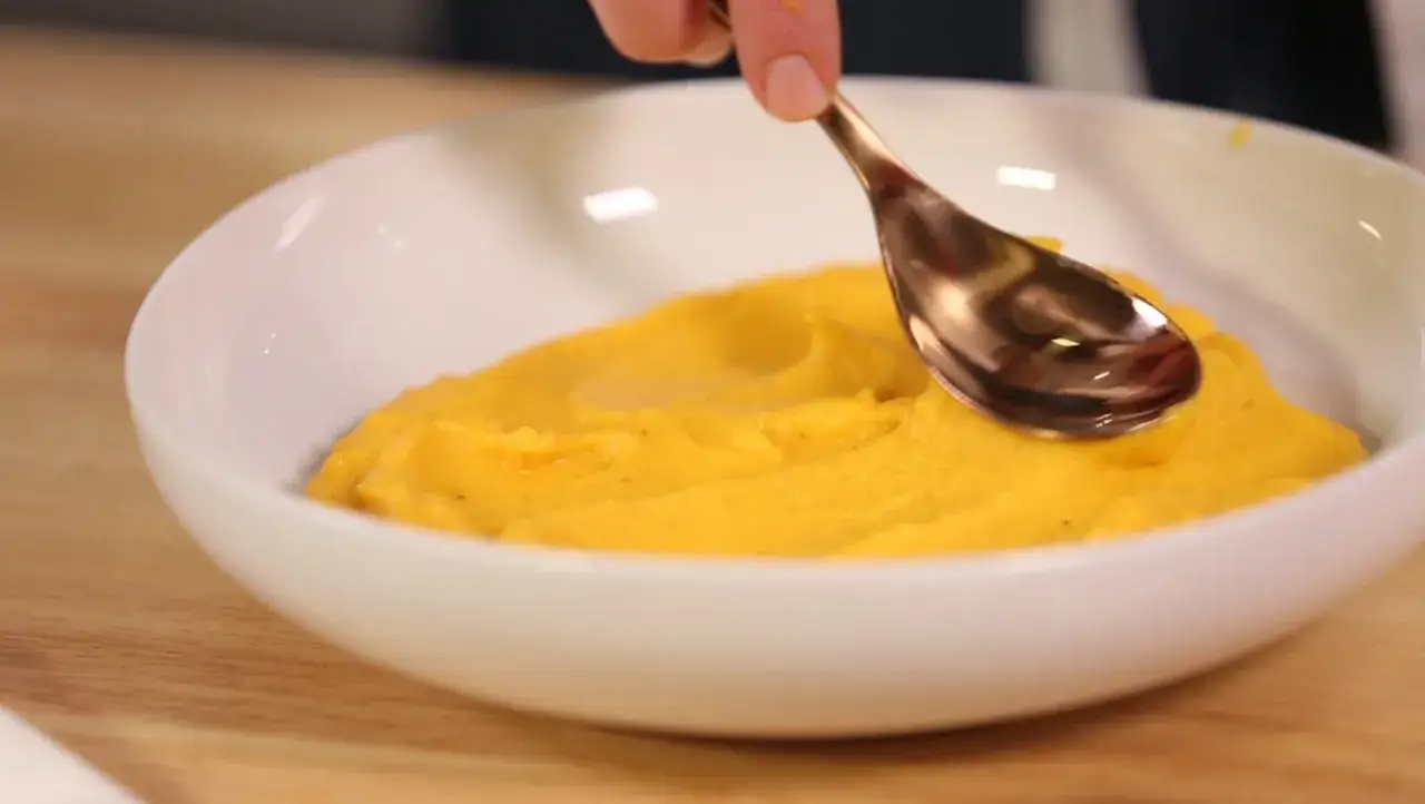 Cuchara sirviendo un cremoso pur&eacute; de verduras thermomix en un cuenco blanco.