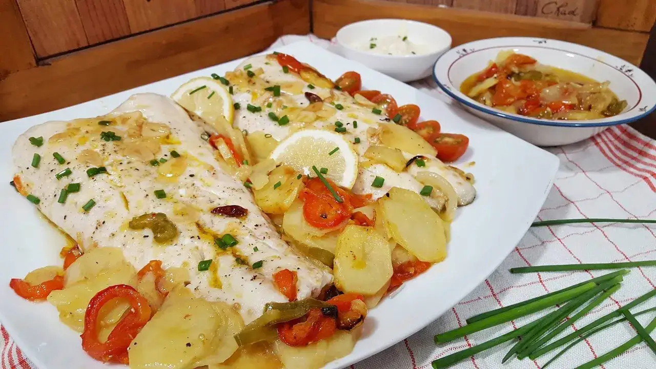 Deliciosa merluza al horno con patatas, pimientos y tomates. Un plato perfecto para disfrutar.