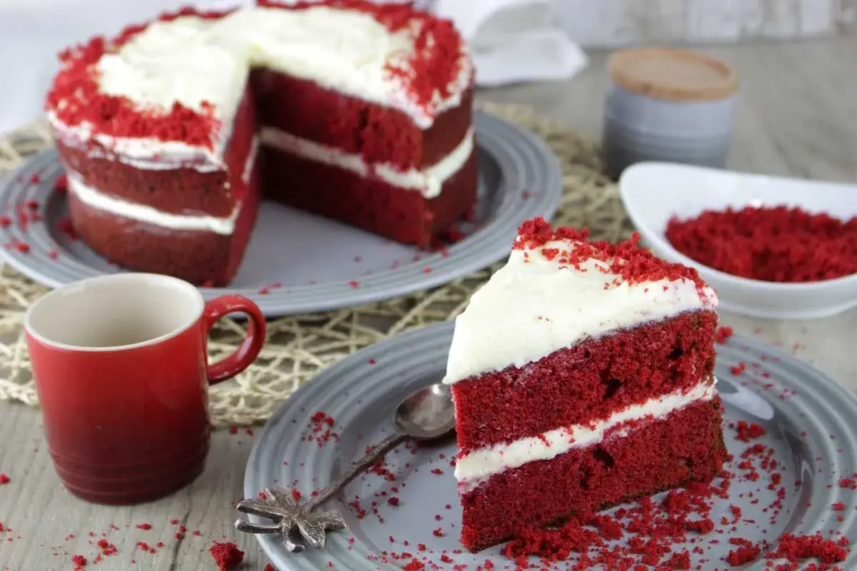 Un delicioso pastel red velvet con capas de bizcocho rojo y crema blanca, decorado con migas rojas.